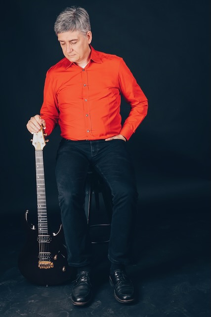 Markus solo auf einem Hocker mit Gitarre daneben